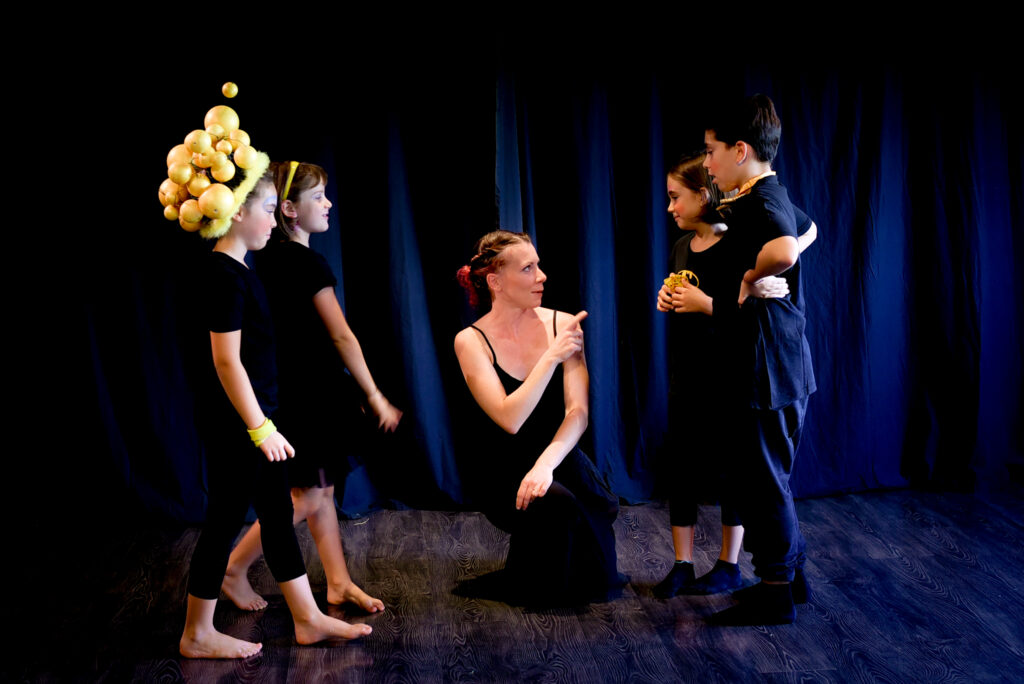 Marta Boscaini inginocchiata a terra spiega una scena agli allievi del corso di teatro 6 8 anni che la circondano