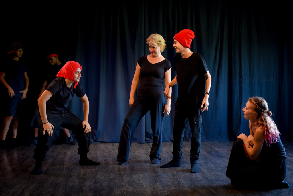 Michela Ottolini e Marta Boscaini provano una scena con due ragazzi del corso di teatro Ragazzi che indossano cappelli rossi
