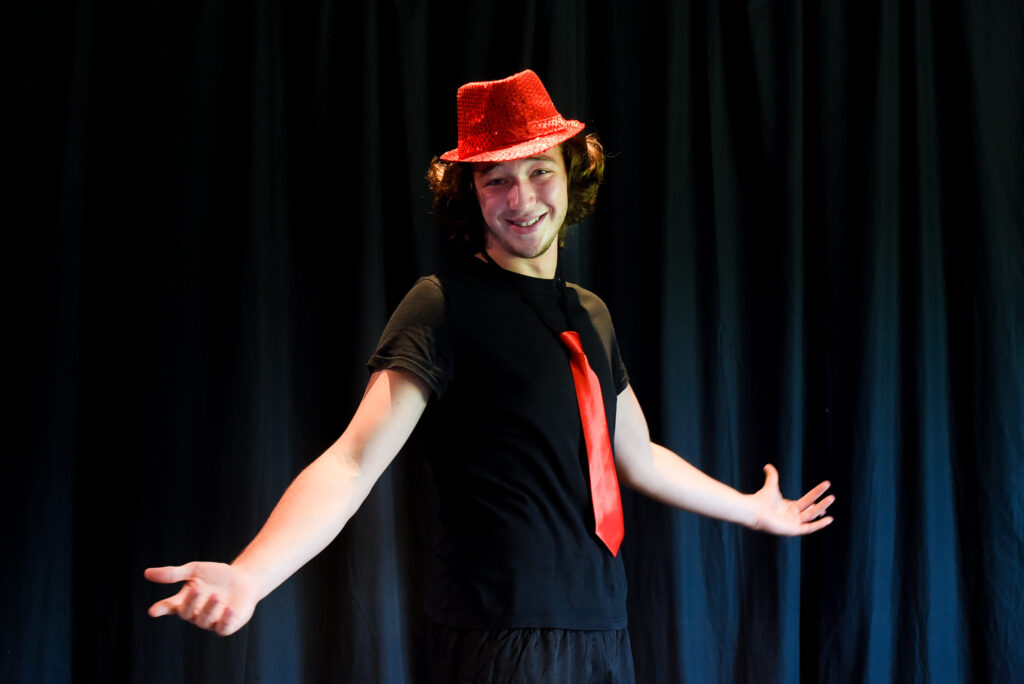 Un allievo del corso di teatro Ragazzi di SpazioMio sorride in scena con cappello e cravatta rossi
